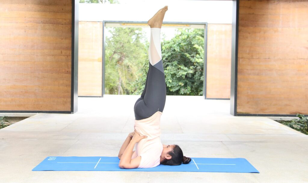 Yoga Sarvangasana - a girl lying on floor with her back stretched upwards