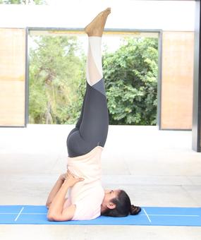 Yoga Sarvangasana - a girl lying on floor with her back stretched upwards