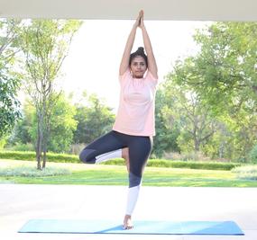 Yoga Vrikshasana - a girl standing with folded hands and one leg bent in tree pose