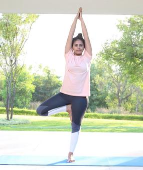 Yoga Vrikshasana - a girl standing with folded hands and one leg bent in tree pose