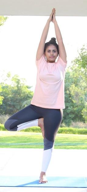 Yoga Vrikshasana - a girl standing with folded hands and one leg bent in tree pose